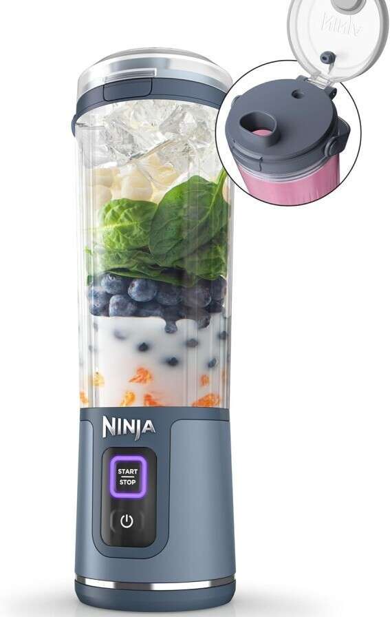 A Ninja personal blender filled with ingredients like ice, spinach, blueberries, and a liquid. It has a blue base with a