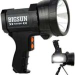 A powerful black and green portable spotlight illuminating a dark forest trail, highlighting its durability and efficiency for camping, hiking, and emergency purposes.